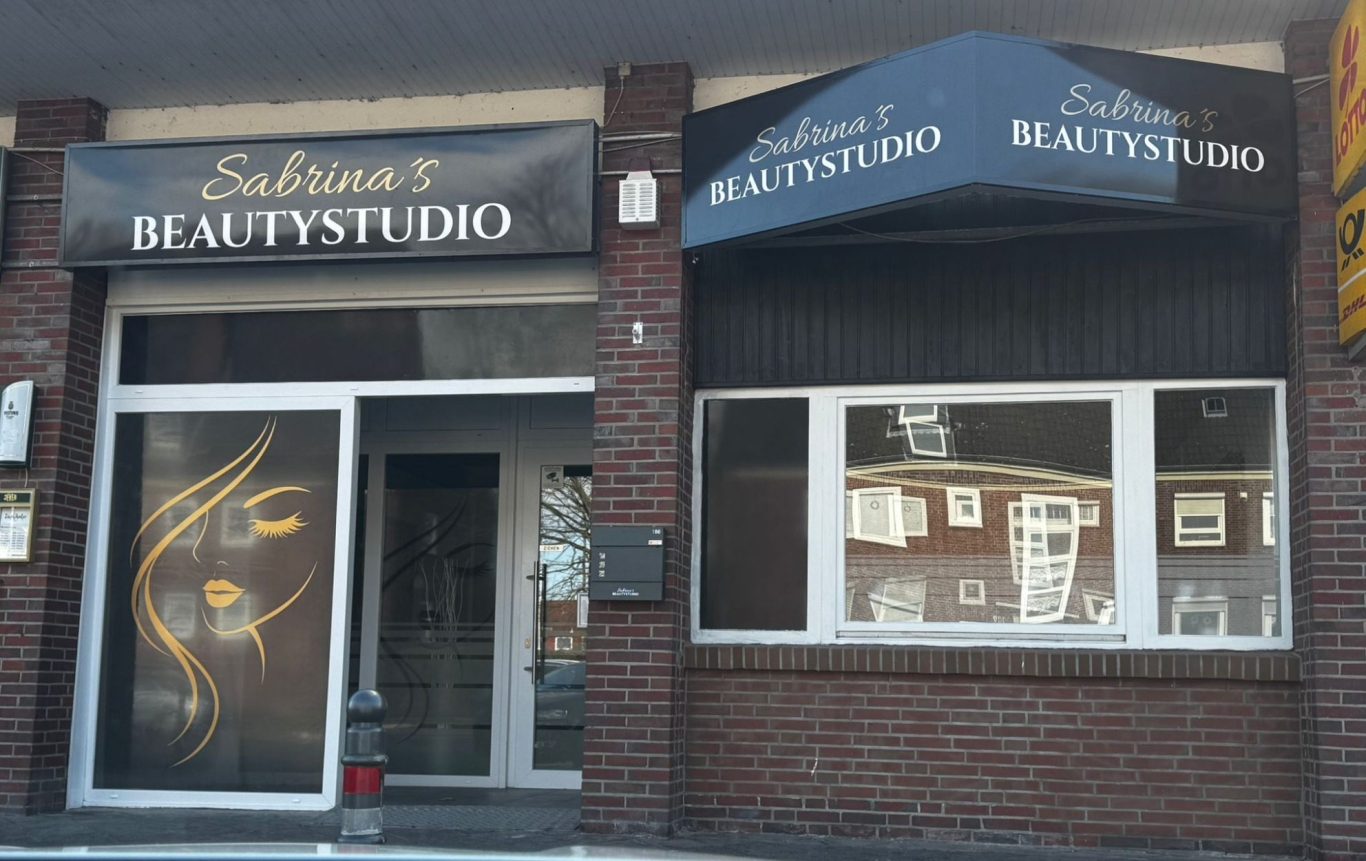 Schaufenster eines Schönheitssalons mit schwarzem Schild und goldenen Akzenten.